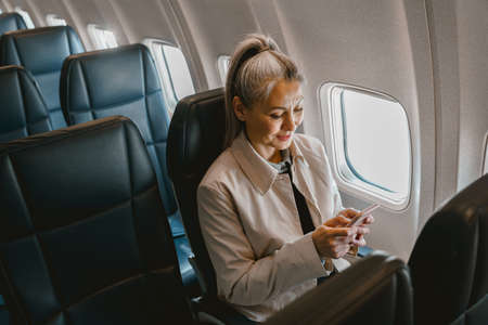 Beautiful Asian woman passenger sitting in the airplane and use phone during boardingの写真素材