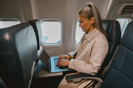 Focused Asian woman passenger sitting in the airplane and working laptop during flightの写真素材