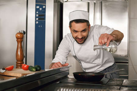 Professional chef pours oil into frying pan for preparing dish on restaurant kitchenの写真素材