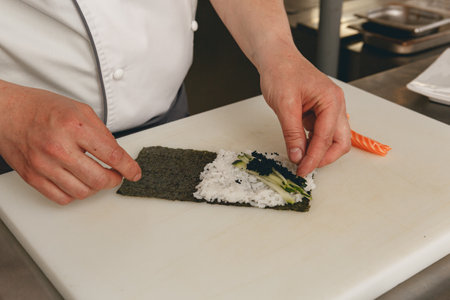 Chef hands cooking sushi with rice, salmon and nori on kitchen of japanese restaurantの写真素材