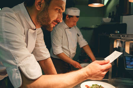 Close up of handsome Chef cook in uniform checking the order at the restaurant kitchen
