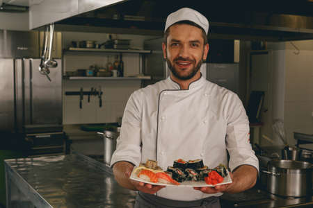 Portrait of cheerful chef standing with cooked traditional japanese sushiの写真素材