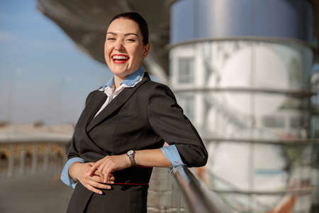 Pretty female flight attendant standing near the terminal and laughingの写真素材