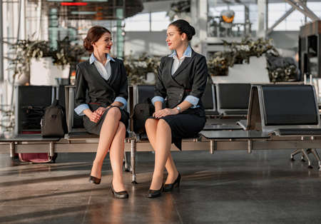 Two flight attendants sitting on the seats and talking in the airport terminalの写真素材