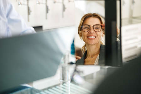 Woman looks in the mirror trying to choose glasses on the advice of an ophthalmologistの写真素材