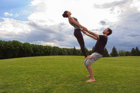 Young healthy couple doing acro yoga in the sunny summer park. Fitness and healthy lifestyle