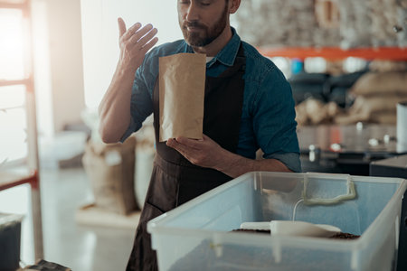 Male Barista in uniform inhaling the aroma of coffee in own manufacturing of roasted coffee beansの写真素材
