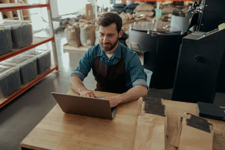 Handsome barista in uniform working laptop on small coffee factoryの写真素材
