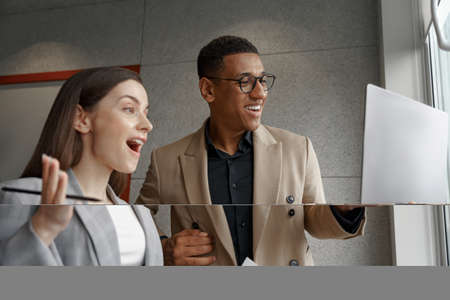 Two surprised business people working with laptop together standing near window