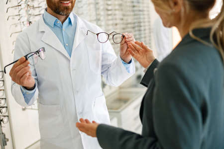 Close up of male optician showing glasses to woman at optics storeの写真素材