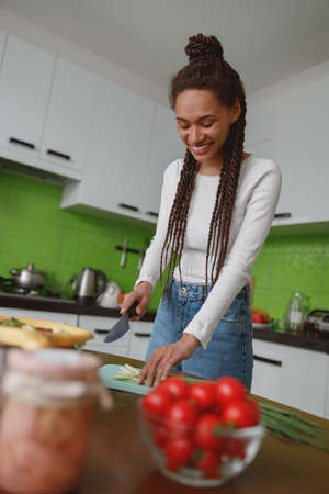 Smiled positive young woman preparing healthy salad chopping green onion in kitchen