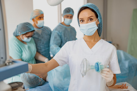 Nurse holding breathing mask for anesthesia standing in operation room with colleagues on backgroundの写真素材
