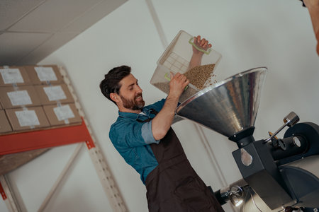 Smiling Entrepreneur pouring raw coffee beans into a modern roasting machine.の写真素材