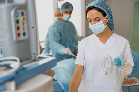 Nurse holding breathing mask for anesthesia standing in operation room with colleagues on backgroundの写真素材