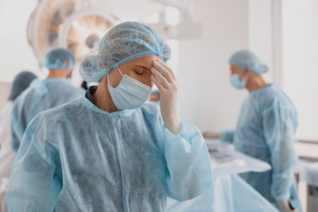 Close up of tired surgeon standing in operating room after hard surgery on background of colleaguesの写真素材