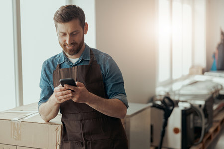 Man worker in uniform standing on coffee warehouse and using mobile phoneの写真素材