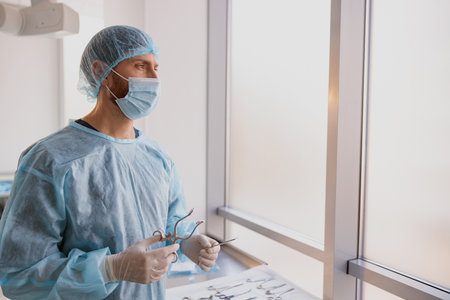 Professional doctor surgeon holding scalpel and forceps in operation room and looking away