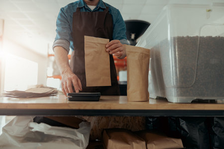 Close up of male worker weighs paper bag with coffee beans on a scale at a coffee factoryの写真素材