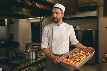 Chef holding tray with baked vegetables while standing in the kitchen of restaurantの写真素材