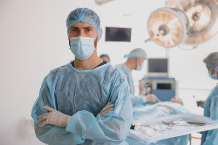 Surgeon in mask standing in operating room with crossing hands, ready to work on patientの写真素材