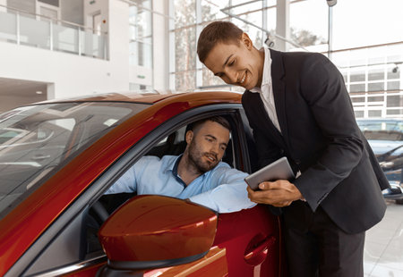 Young male consultant and buyer signing contract for new car in auto showの写真素材