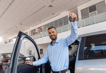 Smiling man customer holding key stands near car in dealership centerの写真素材