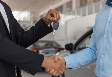 Salesperson giving key to male client at the showroom with modern cars on the backgroundの写真素材