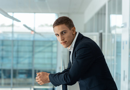 Handsome male businessman standing in auto show office and looking at camera. Blurred backgroundの写真素材