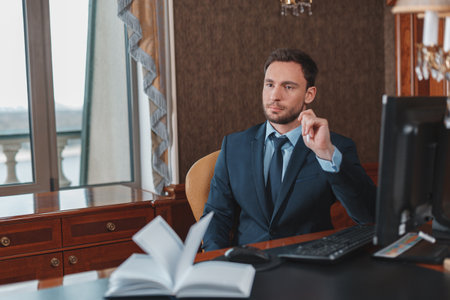 Focused businessman in suit sitting in luxury hotel room and using computerの写真素材