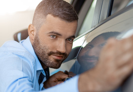 Close up of young smiling man touching and checking new car. Concept for car rentalの写真素材