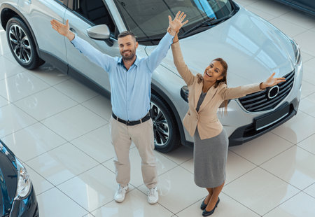 Top view photo of happy couple buying a new car with joyfully raised hands in auto showの写真素材