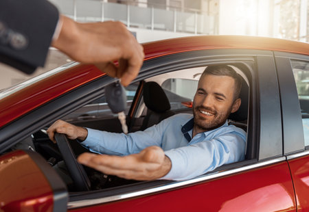Young man sitting inside new car and getting keys to it. Concept for car rentalの写真素材