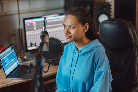 Charming ethnic woman, radio presenter with stylish dreadlocks working in a broadcasting audio recording studioの写真素材
