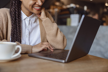 Cropped view to a cute ethnic woman smiling toothy smile while working on laptop during coffee break inside a cafeteriaの写真素材