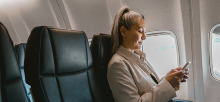 Beautiful Asian woman passenger sitting in the airplane and use phone during boardingの写真素材