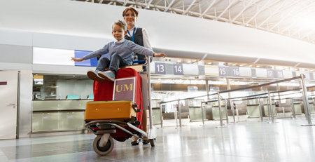 Female airport worker pushes a little boy on a baggage cart through the airport terminalの写真素材