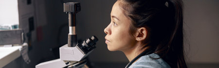 Thoughtful Asian lab assistant sits near microscope looking out of window at workplaceの写真素材