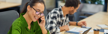 Young cheerful asian woman talking by phone and making some notes while working in the modern officeの写真素材