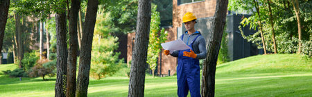 Full length of young builder standing outdoors with blueprint while working on cottage constructionの写真素材