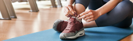 Comfort in everything. Cropped image of sporty woman tying shoelaces while sitting on a mat at gymの写真素材