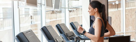 Body improvement. Side view of young and beautiful woman in sportswear running on a treadmill at gym. Cardio workout.の写真素材