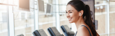 Get faster Side view of young and cheerful woman in sportswear is running on a treadmill at gym and listening music. Cardio workout.の写真素材