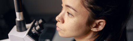 Thoughtful Asian woman in uniform with modern microscope at workplace in hospital laboratoryの写真素材