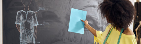 African-American teacher shows blank blue paper against blackboa