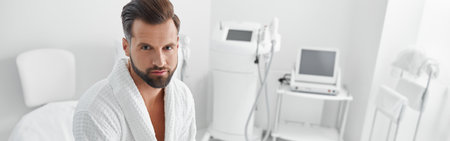 Attractive man in bathrobe with smartphone sits on couch in cosmetologycal salonの写真素材