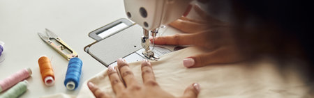 African-American employee sews cloth with machine tool at table in workshopの写真素材
