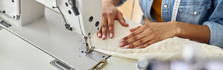 African-American designer blogger sews white fabric with machine at table in studio