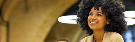 Never stop learning. Happy mixed race woman sitting at desk in the modern coworking space, listening to coach and smiling during corporate trainingの写真素材