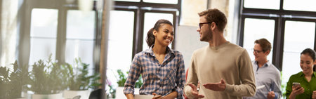 Two young diverse business people, male and female coworkers talking, discussing project and smiling while walking down the modern officeの写真素材