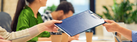 Male coworker giving a folder with documents to his colleague while working in the modern office